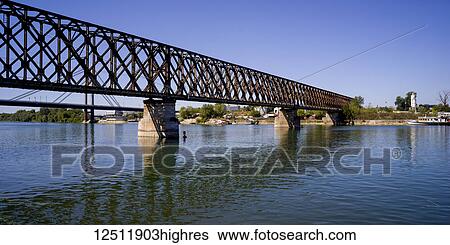 Stock Photograph - A bridge crossing the Sava River reflected in the water with blue sky; Belgrade, Vojvodina, Serbia. Fotosearch