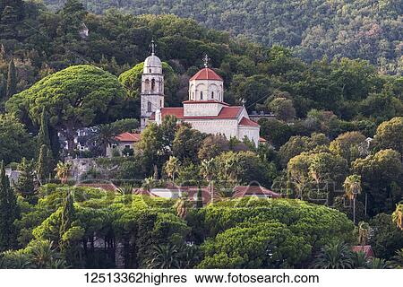 Stock Photograph - A church and buildings on a hillside surrounded by trees; Herceg Novi, Monte. Fotosearch