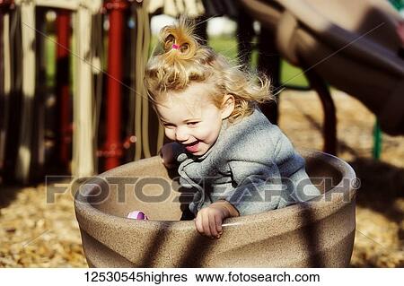 Stock Photograph - A cute young girl spinning in a saucer on a playground during the fall season; Spruce Grove, Alberta, Canada. Fotosearch