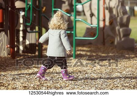 Stock Photograph - A cute young girl walking in a playground in her rubber boots during the fall season; Spruce Grove, Alberta, Canada. Fotosearch