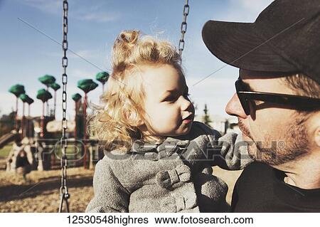 Stock Photograph - A cute young girl with her father after playing in a playground during the fall season; Spruce Grove, Alberta, Canada. Fotosearch