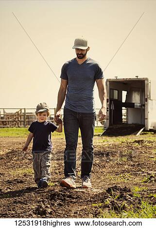 Stock Photograph - A father walks and holds hands with his young son on a farm; Edmonton, Alberta, Canada. Fotosearch