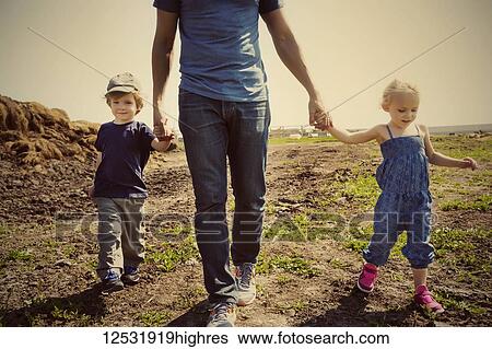 Stock Photograph - A father walks and holds hands with his young son and daughter on a farm; Edmonton, Alberta, Canada. Fotosearch