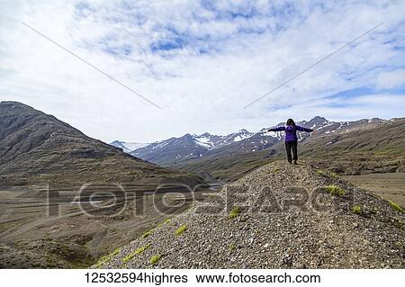 Stock Photograph - A female hiker celebrates nature with her arms outstretched at the peak of a hill in the mountain landscape of Southern Iceland; Iceland. Fotosearch