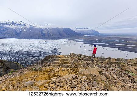A female hiker in warm clothing for the elements stands on the edge of moutain cliff overlooking the glacier lake and valley views of Vatnajokull National Park; Iceland View Large Photo Image Stock Photograph - A female hiker in warm clothing for the elements stands on the edge of moutain cliff overlooking the glacier lake and valley views of Vatnajokull National Park; Iceland. Fotosearch