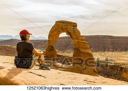 A female hiker sits enjoying the view of Delicate Arch in Arches National Park; Moab, Utah, United States of America View Large Photo Image Stock Photograph - A female hiker sits enjoying the view of Delicate Arch in Arches National Park; Moab, Utah, United States of America. Fotosearch