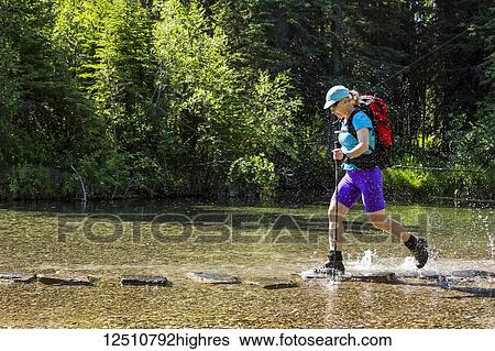 A female hiker with trekking poles leaps from rock to rock in a shallow stream and splashes water with her boots; Calgary, Alberta, Canada View Large Photo Image Stock Photograph - A female hiker with trekking poles leaps from rock to rock in a shallow stream and splashes water with her boots; Calgary, Alberta, Canada. Fotosearch