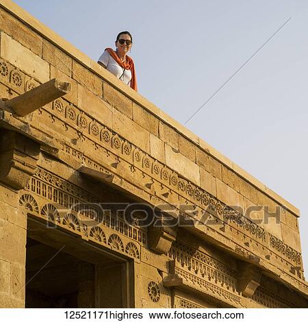 Stock Photograph - A female tourist looks down from a rooftop in the abandoned village of Kuldhara in the Jaisalmer district, having a reputation of being haunted; Jiyai, Rajasthan, India. Fotosearch