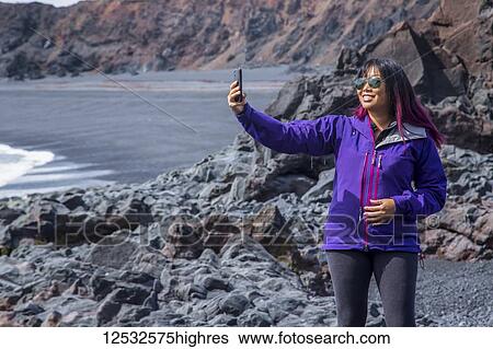 A female tourist poses for a self-portrait with her phone on the black sand beach in Western Iceland, Snaefellsnes peninsula; Iceland View Large Photo Image Stock Photograph - A female tourist poses for a self-portrait with her phone on the black sand beach in Western Iceland, Snaefellsnes peninsula; Iceland. Fotosearch