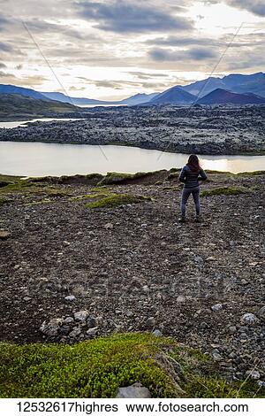 Stock Photograph - A female tourist poses on the edge of a hilltop overlooking a vast river valley in Western Iceland; Iceland. Fotosearch