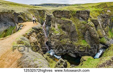 Stock Photograph - A female tourist stands on a cliff viewpoint in the picturesque valley of Fjadrargljufur in Southern Iceland; Iceland. Fotosearch