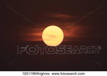 A glowing yellow sun sinking in a dark sky with red clouds; Lake of the Woods, Ontario, Canada View Large Photo Image Stock Photograph - A glowing yellow sun sinking in a dark sky with red clouds; Lake of the Woods, Ontario, Canada. Fotosearch