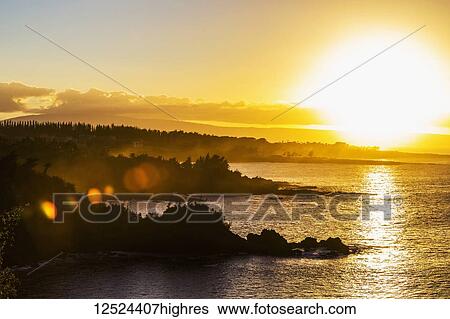 Stock Photograph - A golden sunset casting yellow light over the ocean and coastline near Honolua Bay; Kaanapali, Maui, Hawaii, United States of America. Fotosearch