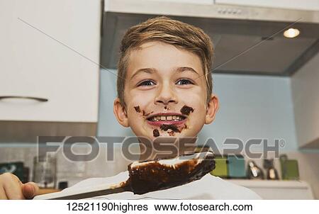 Stock Photograph - A grinning young boy with a messy face licks the chocolate from the spatula after making fudge; Langley, British Columbia, Canada. Fotosearch