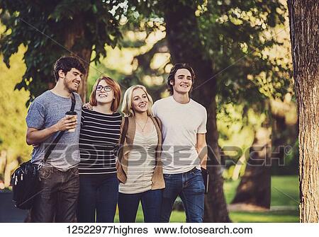 Stock Photograph - A group of four friends walk closely together arm in arm down a path while talking and laughing on a university campus; Edmonton, Alberta, Canada. Fotosearch
