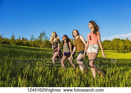 Stock Photograph - A group of four girlfriends hike together through a field in a park; Edmonton, Alberta, Canada. Fotosearch