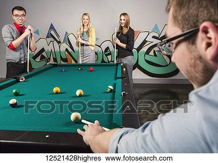 Stock Photograph - A group of young millennial business professionals playing a game of pool together on a work break; Sherwood Park, Alberta, Canada. Fotosearch