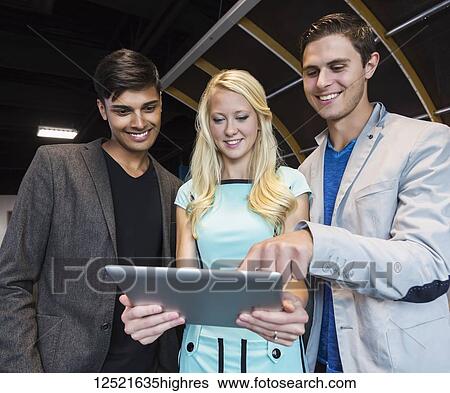 Stock Photograph - A group of young millennial business professionals in the workplace using technology; Sherwood Park, Alberta, Canada. Fotosearch