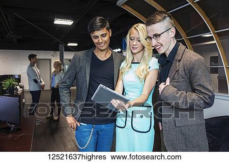 Stock Photograph - A group of young millennial business professionals in the workplace using technology; Sherwood Park, Alberta, Canada. Fotosearch