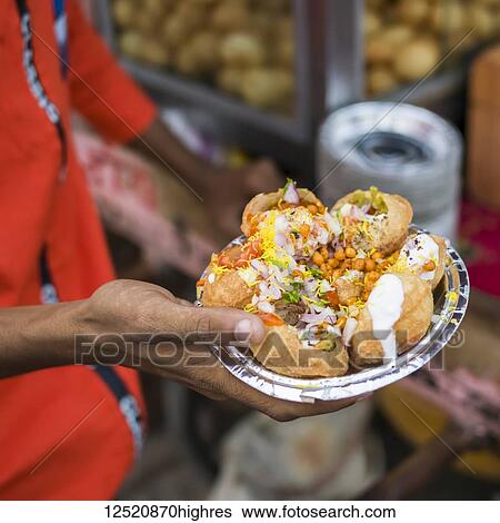 Stock Photograph - A hand holding a foil plate with a serving of traditional Indian food; Jaipur, Rajasthan, India. Fotosearch
