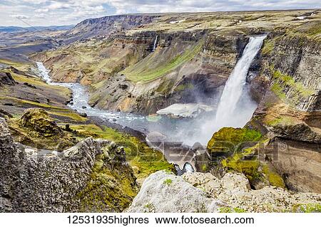 Stock Photograph - A high viewpoint of one of the waterfalls and rivers in the Haifoss valley with stunning cliffs, natural colors and rock formations; Iceland. Fotosearch