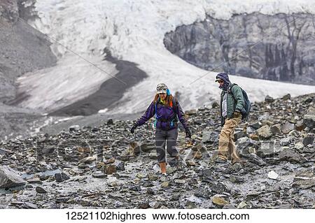 Stock Photograph - A husband and wife hike on the rugged surface of Gulkana Glacier; Alaska, United States of America. Fotosearch