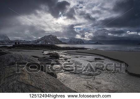 Stock Photograph - A landscape with rugged mountains and sand along the coastline under a cloudy sky; Nordland, Norway. Fotosearch