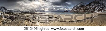 Stock Photograph - A landscape with rugged mountains and sand along the coastline under a cloudy sky; Nordland, Norway. Fotosearch