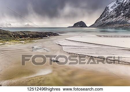 Stock Photograph - A landscape with rugged mountains and sand along the coastline under a cloudy sky; Nordland, Norway. Fotosearch