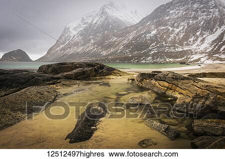 Stock Photograph - A landscape with rugged mountains and sand along the coastline under a cloudy sky; Nordland, Norway. Fotosearch
