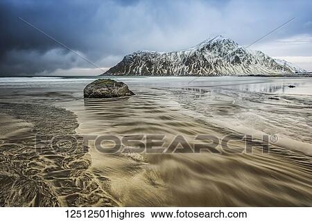 Stock Photograph - A landscape with rugged mountains and sand along the coastline under a cloudy sky; Nordland, Norway. Fotosearch
