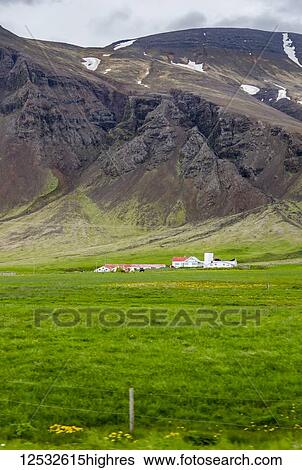 Stock Photograph - A large farmhouse estate property surrounded by vast fields in front of volcanic hillsides; Iceland. Fotosearch