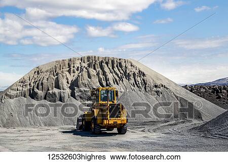 Stock Photograph - A large wheel loader heavy equipment machine is parked in front of a gravel pile in the mountain landscape; Iceland. Fotosearch