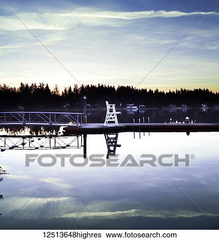 Stock Photograph - A lifeguard chair on the dock of a tranquil lake at sunrise, Lakeside Bible Camp; Whidbey Island, Washington, United States of America. Fotosearch