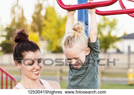 A little girl with blonde hair playing in in a playground on a warm fall day while her mom watches to keep her safe; Spruce Grove, Alberta, Canada View Large Photo Image Stock Photograph - A little girl with blonde hair playing in in a playground on a warm fall day while her mom watches to keep her safe; Spruce Grove, Alberta, Canada. Fotosearch