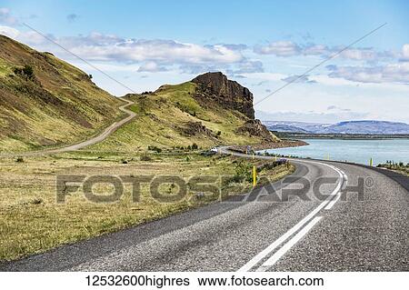 Stock Photograph - A long winding road leading into the hills in Iceland where open paved roads lead throughout the volcanic landscape to views across the country; Iceland. Fotosearch