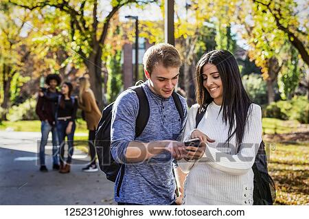 A male and female university student stand on a path looking at a smart phone together with a group of fellow students in the background; Edmonton, Alberta, Canada View Large Photo Image Stock Photograph - A male and female university student stand on a path looking at a smart phone together with a group of fellow students in the background; Edmonton, Alberta, Canada. Fotosearch
