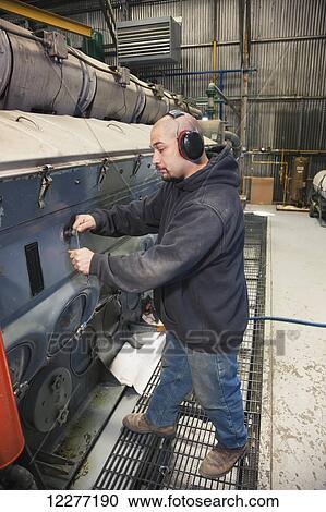 Stock Image - A male Hispanic worker repairs a diesel generator inside an electrical power plant, Prudhoe Bay, Arctic Alaska, USA, Summer. Fotosearch