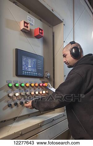 Stock Image - A Male laborer wearing ear protection inspects an electrical power plant control panel, Prudhoe Bay, Arctic Alaska, USA, Summer. Fotosearch