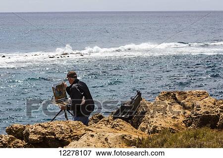 A man on the seashore painting a coastal scene from an easel; Poipu, Kauai, Hawaii, United States of America View Large Photo Image Stock Photo - A man on the seashore painting a coastal scene from an easel; Poipu, Kauai, Hawaii, United States of America. Fotosearch