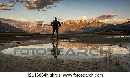 A man stands with his reflection in a pool of water looking out over the Saint Elias Mountains at sunset, Kluane National Park and Reserve; Destruction Bay, Yukon, Canada View Large Photo Image Stock Photograph - A man stands with his reflection in a pool of water looking out over the Saint Elias Mountains at sunset, Kluane National Park and Reserve; Destruction Bay, Yukon, Canada. Fotosearch