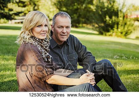 A middle-aged couple sitting on the grass in a park just before sunset and the husband is looking at the camera; At. Albert, Alberta, Canada View Large Photo Image Stock Photograph - A middle-aged couple sitting on the grass in a park just before sunset and the husband is looking at the camera; At. Albert, Alberta, Canada. Fotosearch