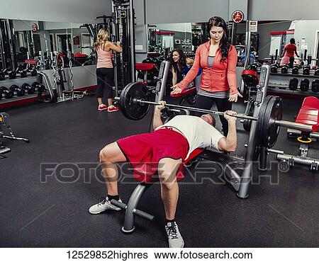 Stock Photograph - A middle-aged man doing a bench press at a fitness facility while being spotted by his personal trainer; Spruce Grove, Alberta, Canada. Fotosearch