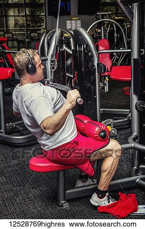 Stock Photograph - A middle-aged man working out doing pulldowns on a universal machine at a fitness facility; Spruce Grove, Alberta, Canada. Fotosearch