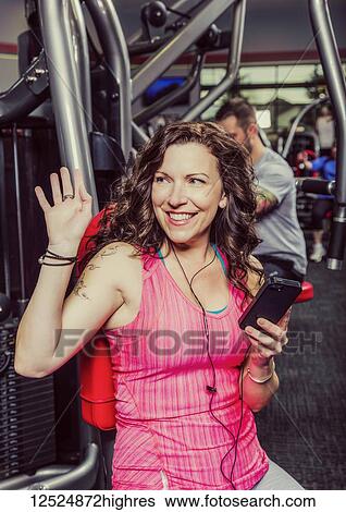 Stock Photograph - A middle-aged woman working out at a fitness facility and waving to someone she recognizes; Spruce Grove, Alberta, Canada. Fotosearch