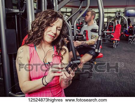 Stock Photograph - A middle-aged woman working out at a fitness facility and and listening to music on her smart phone; Spruce Grove, Alberta, Canada. Fotosearch