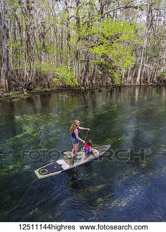 Stock Photograph - A mother and daughter paddleboard down the stream of freshwater spring; Chiefland, Florida, United States of America. Fotosearch