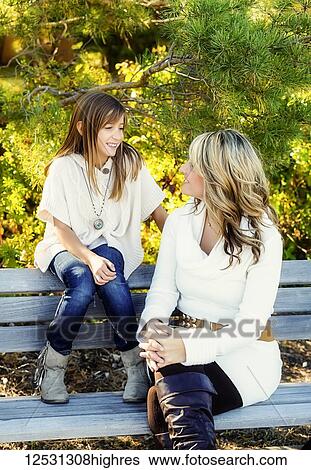 Stock Photograph - A mother and daughter sitting on a park bench talking and enjoying each other's company on a warm fall day; Edmonton, Alberta, Canada. Fotosearch