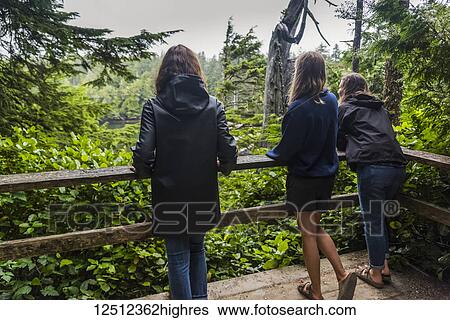 Stock Photograph - A mother and her two daughters stand on a viewing platform looking out to the lush rainforest; Ucluelet, British Columbia, Canada. Fotosearch