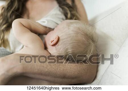 Stock Photograph - A mother holds her young baby girl and breastfeeds her on her bed; Sorrento, British Columbia, Canada. Fotosearch